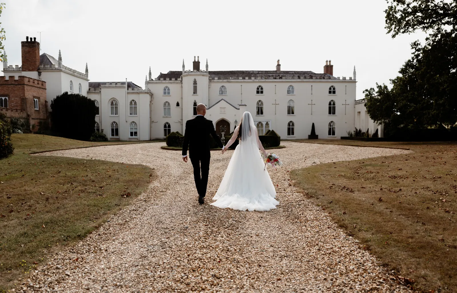 Bride and groom walking hand in hand up the gravel drive to a country house wedding venue
